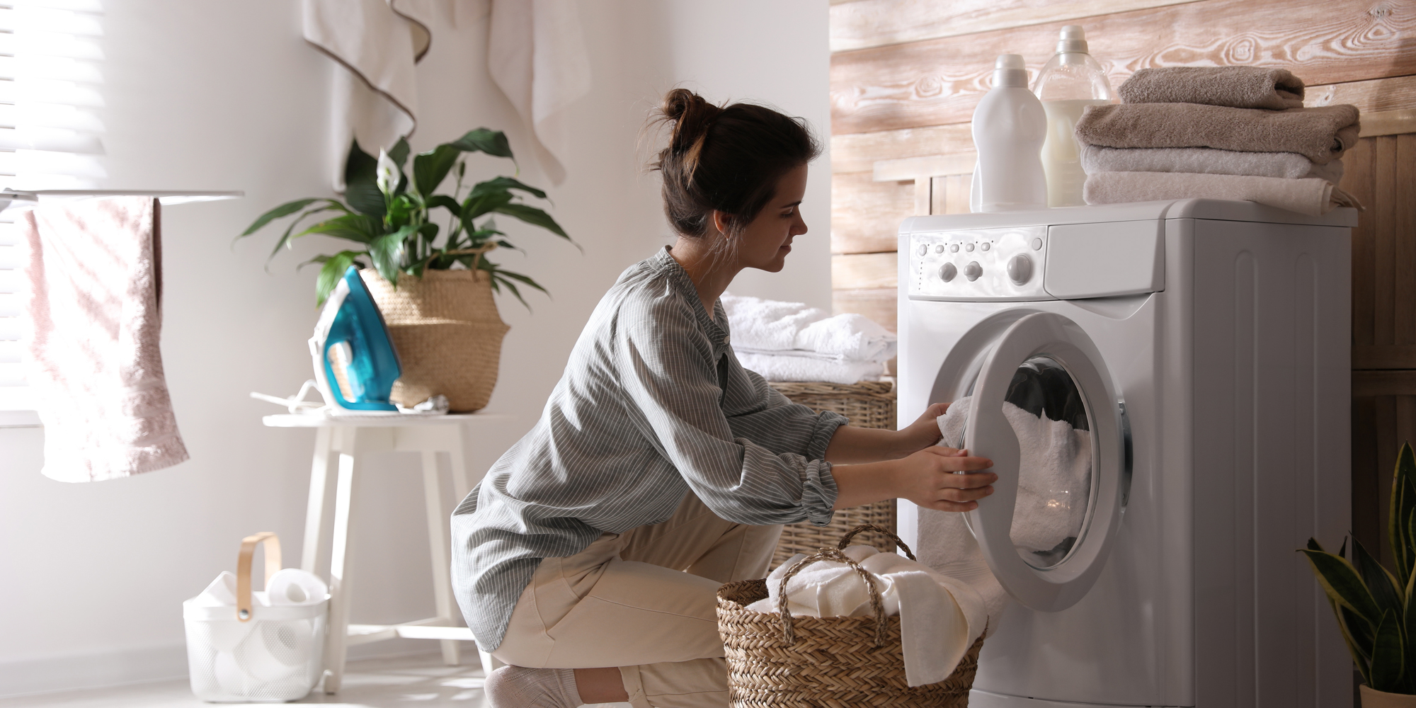 Kvinde lægger tøj i vaskemaskine, som er en af de elapparater i hjemmet, som bruger meget strøm